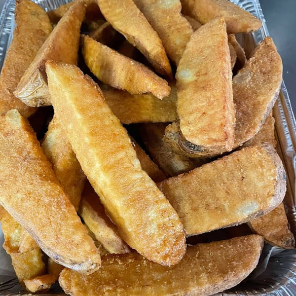 A close-up of golden-brown, crispy potato wedges in a foil container from The Original Village Pizza.