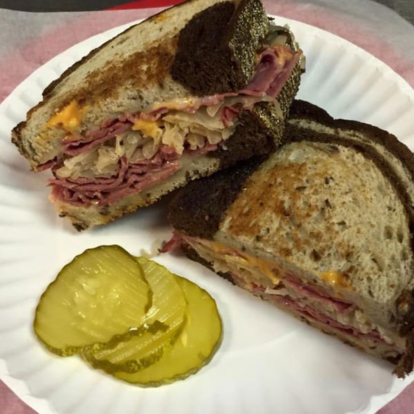 A Reuben sandwich with corned beef, sauerkraut, and cheese on rye bread, with pickle slices.