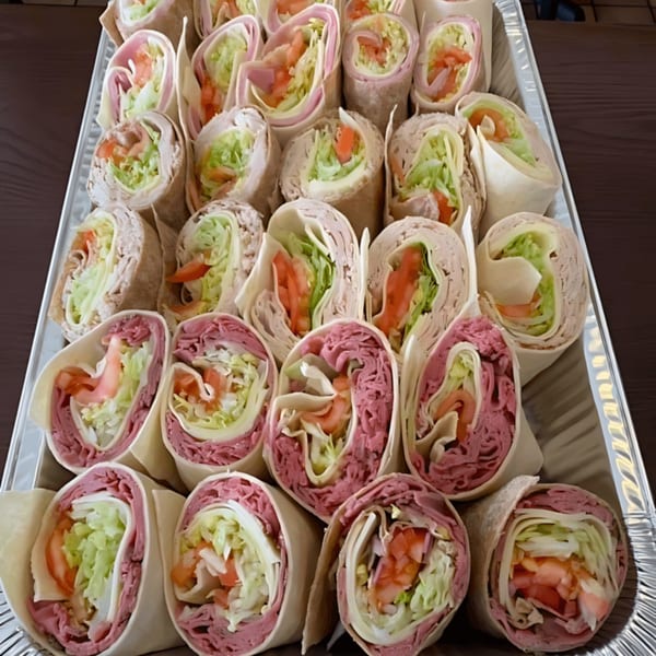 A catering tray filled with various wraps, including ham, turkey, and roast beef.