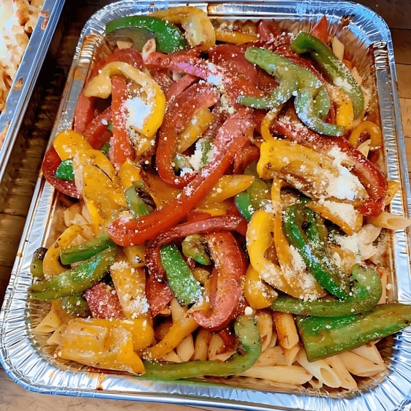 Colorful bell peppers and pasta in a foil tray, topped with grated cheese.