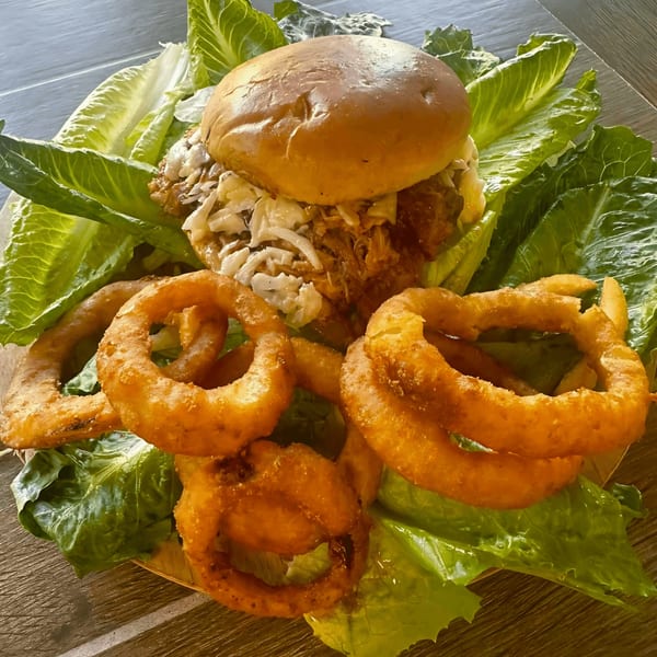 Pulled pork sandwich with coleslaw and onion rings on a bed of lettuce.