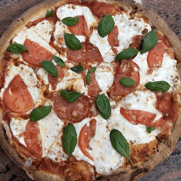 A freshly baked Original Village Pizza Margherita, topped with melted mozzarella, sliced tomatoes, and basil.