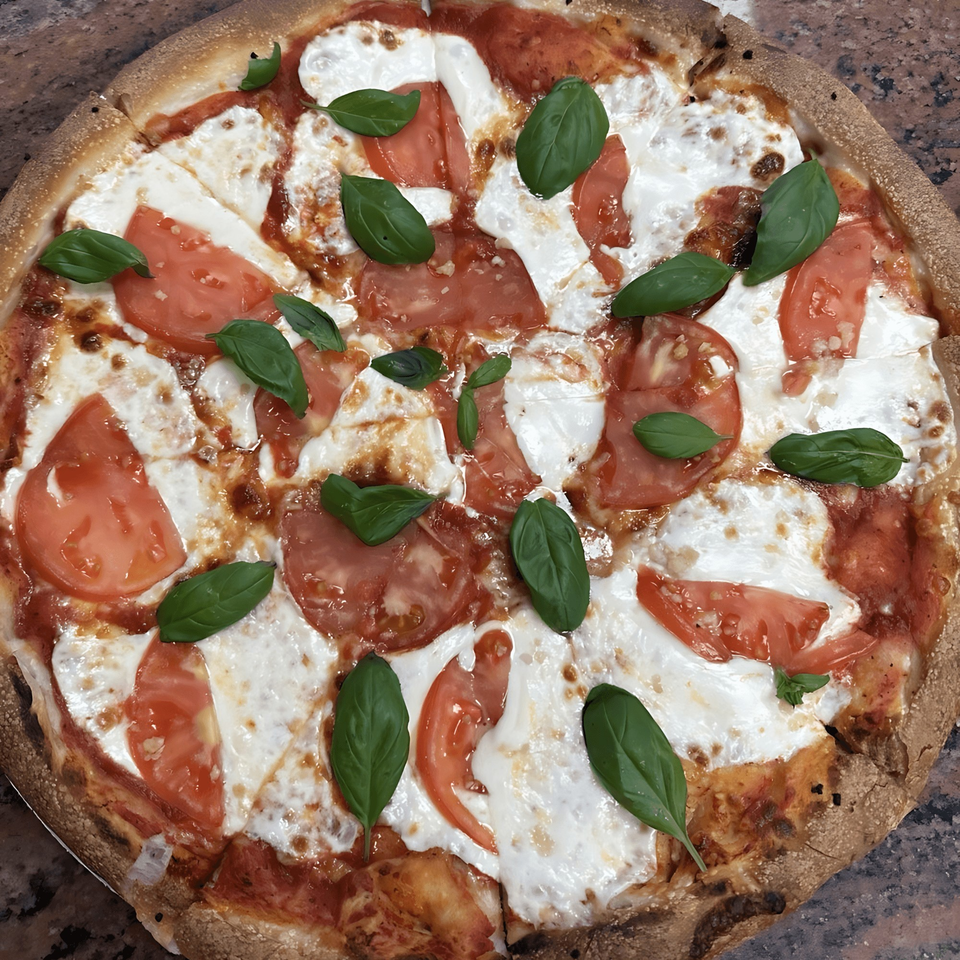 A freshly baked Original Village Pizza Margherita, topped with melted mozzarella, sliced tomatoes, and basil.