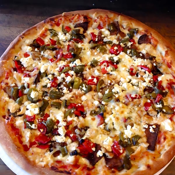 A whole pizza from The Original Village Pizza, topped with red and green peppers, and feta cheese.